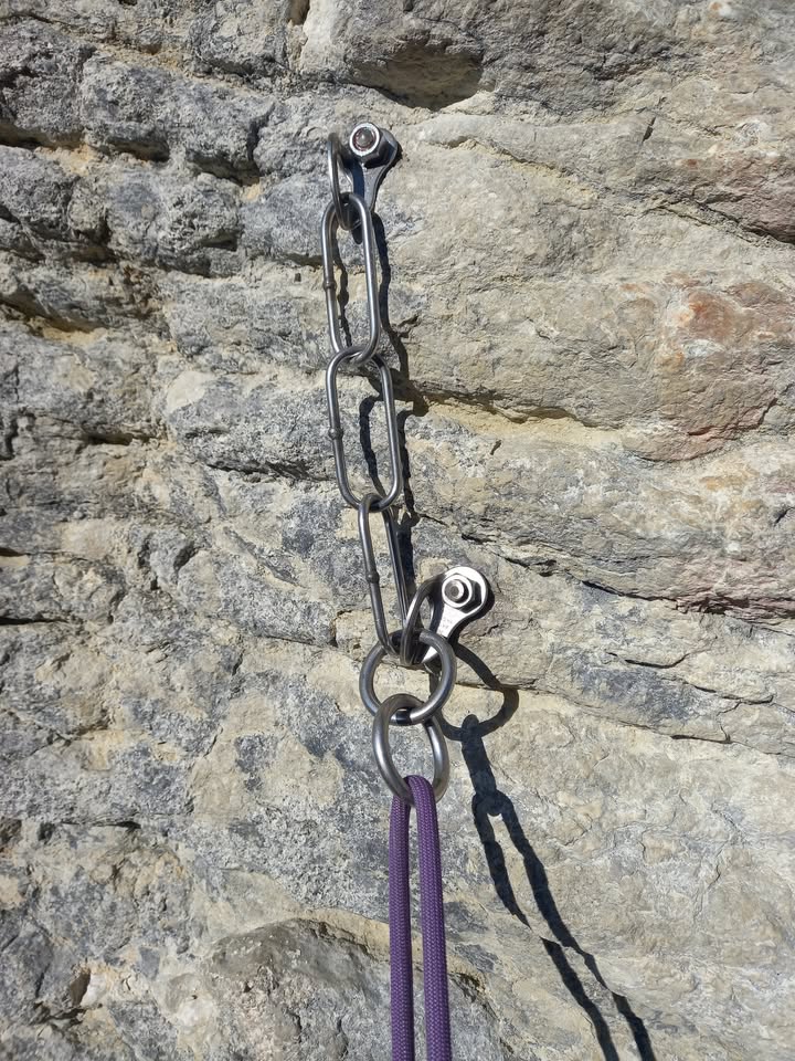 A new stainless steel anchor on the limestone, with a purple rope clipped in