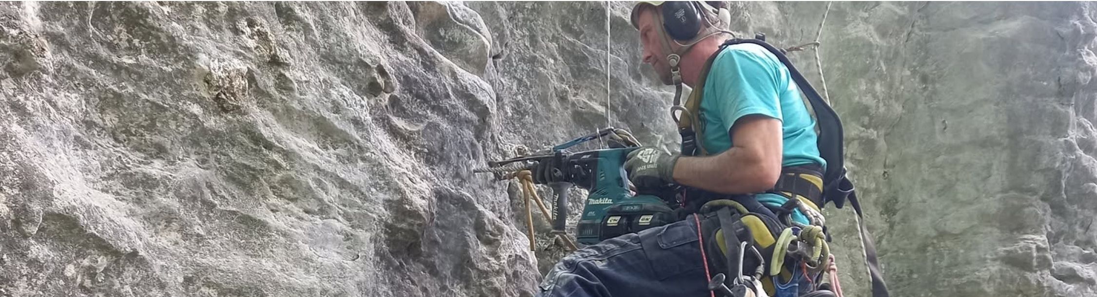 A volunteer hanging on a rope, drilling a new bolt hole in the limestone